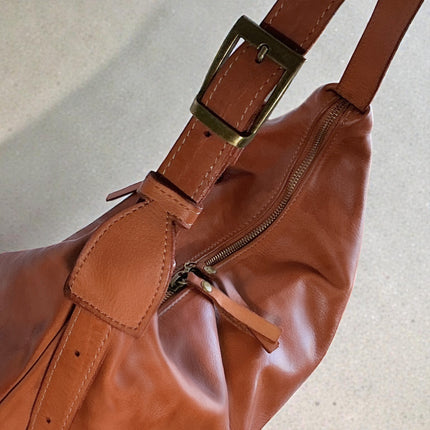 Brown leather handbag with an antique gold tone strap buckle on a light background