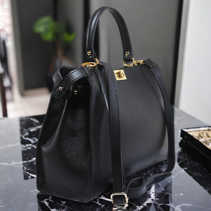 Black leather handbag with gold tone fittings on a marble surface