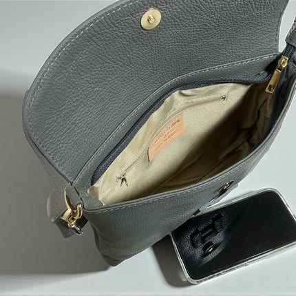 Gray leather open handbag with a phone beside it on a light gray background