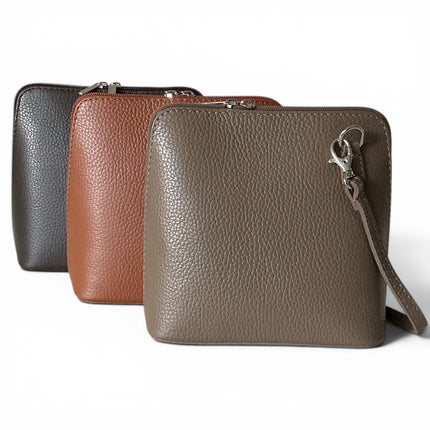 Three pebbled leather zip-around crossbody bags in black, dark tan and dark taupe, arranged in a row on a white background.
