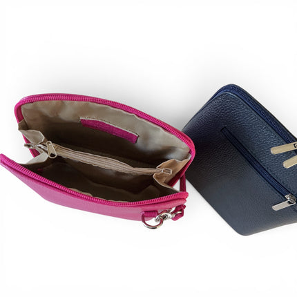 Two zip-around crossbody bags on a white background, one open in bright fuchsia showing a beige interior and the other closed in navy showing a textured navy exterior and back zip.