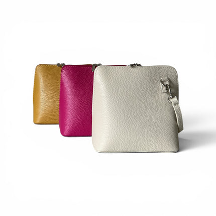 Three small pebbled leather crossbody pouches in mustard, fuchsia and cream, arranged in a diagonal row on a white background.