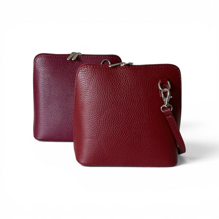 Two pebbled leather zip-around crossbody bags in wine and plum, both featuring silver tone hardware and an adjustable strap, set against a clean white background.