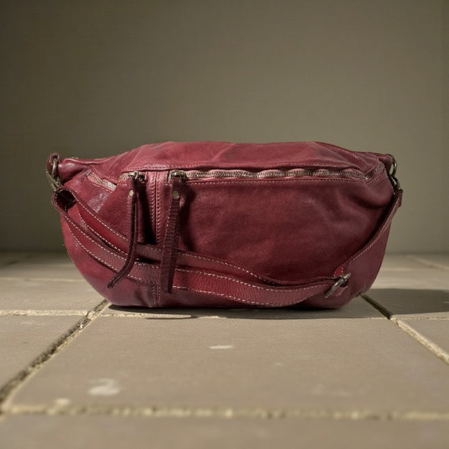 Maroon leather sling bag on a tiled floor with a neutral background