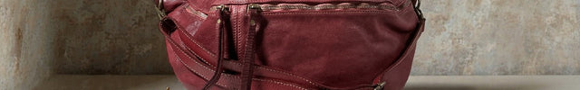Burgundy leather bag on a wooden surface with a textured wall background
