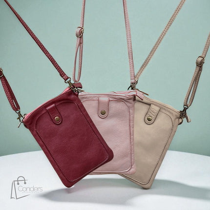 Three leather crossbody bags in red, pink, and beige on a light blue background.