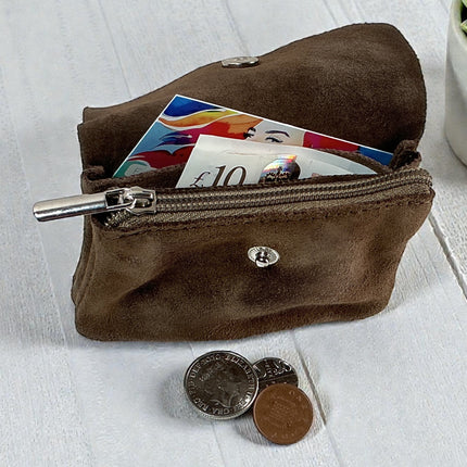 Brown suede coin purse with coins and banknotes on a light wooden surface.