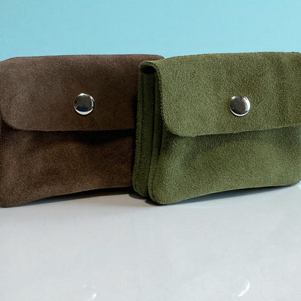 Two suede coin pouches, one brown and one green, on a reflective surface with a light blue background.