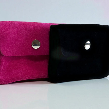 Pink and black suede coin purses on a reflective surface with a light gray background